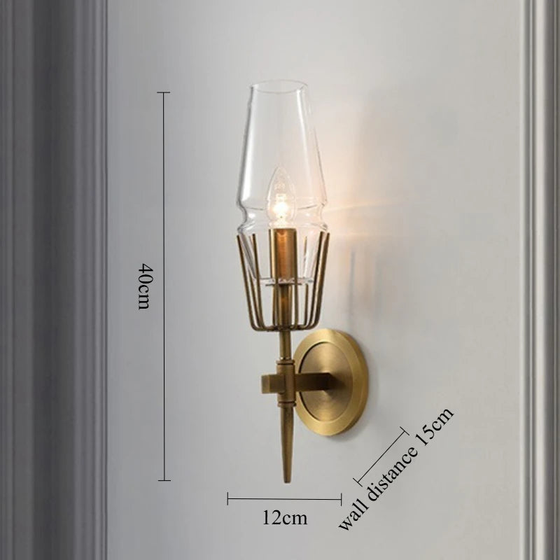 Wall-mounted brass sconce with clear glass shade on a gray wall, showing dimensions.