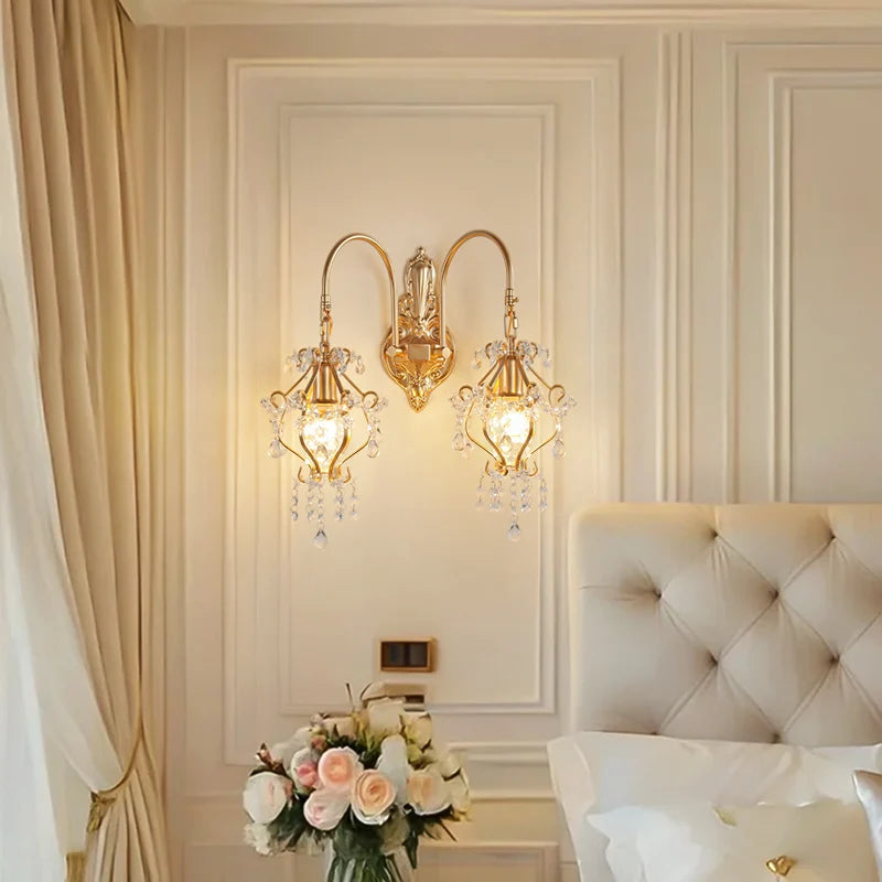 Luxurious bedroom with gold wall sconces, white bed, and floral arrangement.
