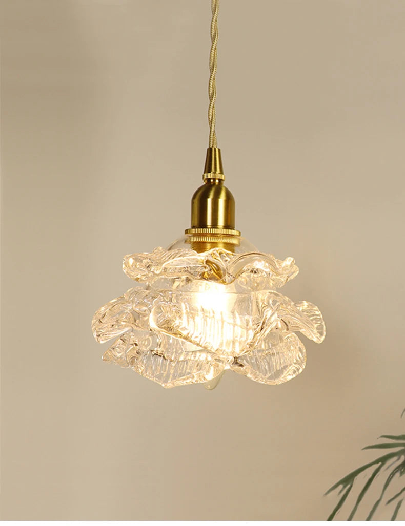Close-up of a brass-finished pendant light with a clear glass shade shaped like a blooming flower.