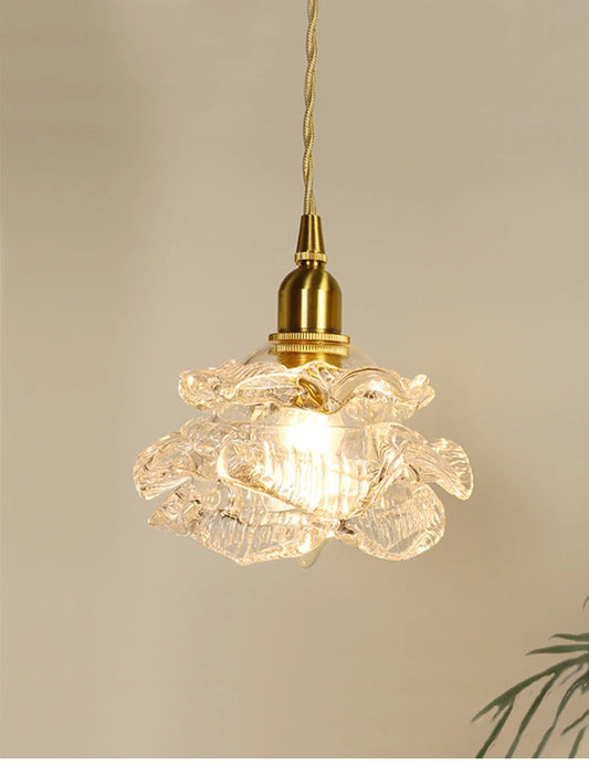 Close-up of a brass-finished pendant light with a clear glass shade shaped like a blooming flower.