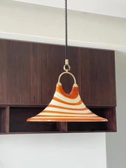 Orange and white striped horn-shaped pendant light hanging from a black cord against a dark wood cabinet background.