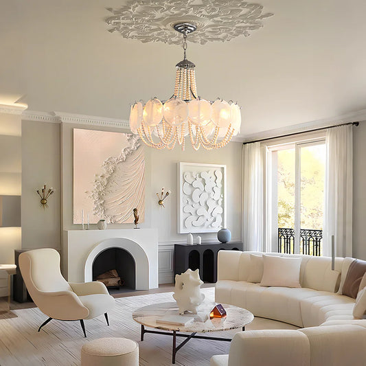 A grand gold chandelier with cascading pearl strings and translucent white glass shades, illuminating a luxurious living room.