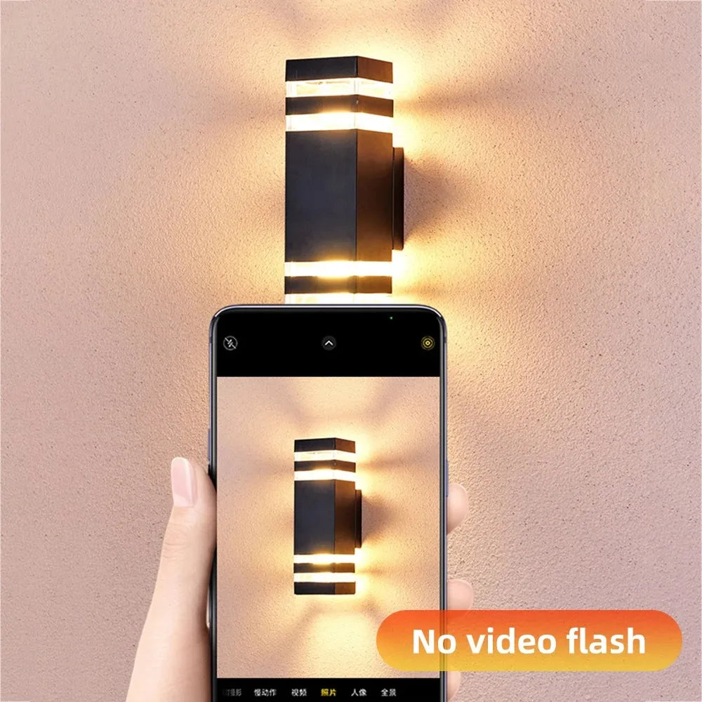 Hand holding a smartphone taking a photo of a wall-mounted light fixture with 'No video flash' text.