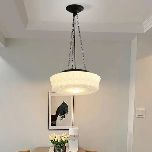 Cream decorative glass pendant light with a black chain hanging in a dining room above a table.