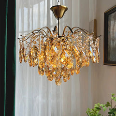 Gold chandelier with crystal accents hanging in a room with curtains and a plant.