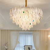 A tiered chandelier with clear crystal leaf accents and colorful gem details, suspended from a gold cord.