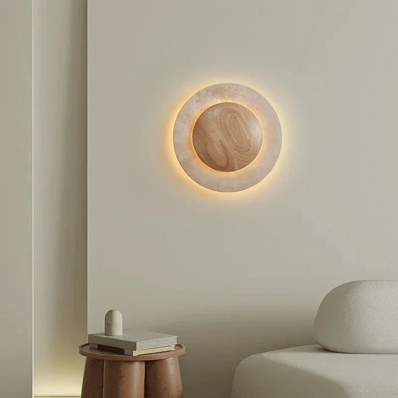 Close-up of a round stone wall sconce with a warm LED glow, set against a neutral-toned wall, with a small wooden side table and decorative object nearby.