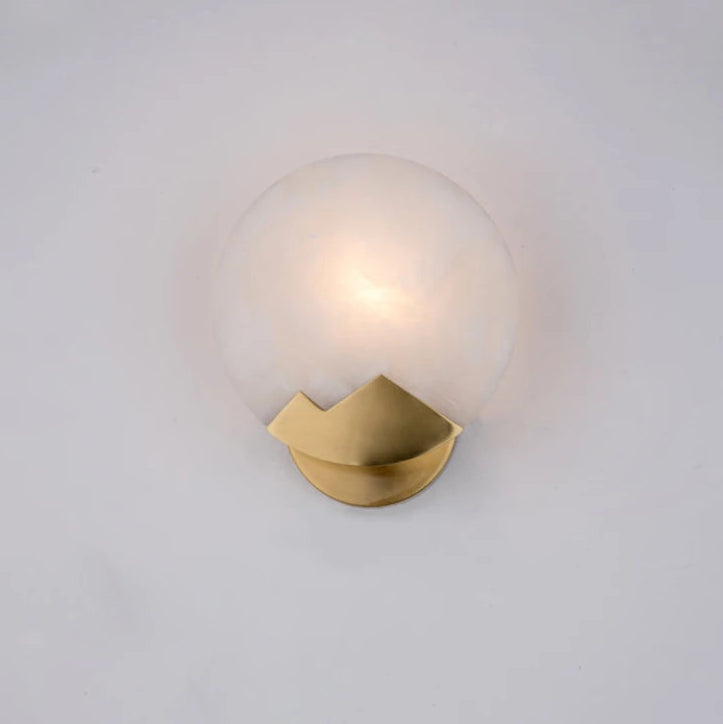 Wall-mounted light fixture with gold base and glass shade on a white background