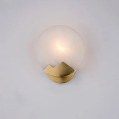 Wall-mounted light fixture with gold base and glass shade on a white background