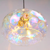 Close-up of a clear glass pendant light with iridescent, wavy textures and a gold-colored central fixture, reflecting colorful light.