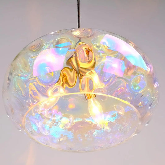 Close-up of a clear glass pendant light with iridescent, wavy textures and a gold-colored central fixture, reflecting colorful light.