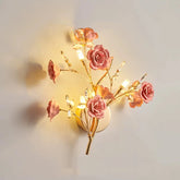 A gold wall sconce with pink ceramic flowers and clear crystals, emitting a warm light.
