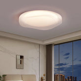 Ceiling view of a modern white textured LED flush mount light fixture in a bedroom with soft illumination.
