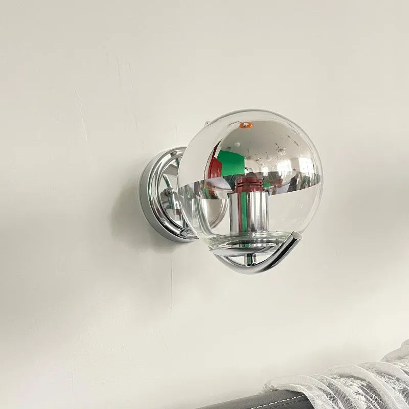 Wall-mounted light fixture with a reflective glass cover on a plain background