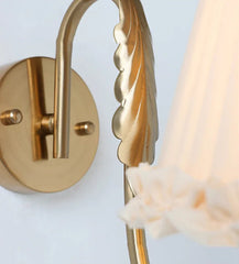 french retro wall lamp with pleated fabric shade and brass arm mounted on white wall