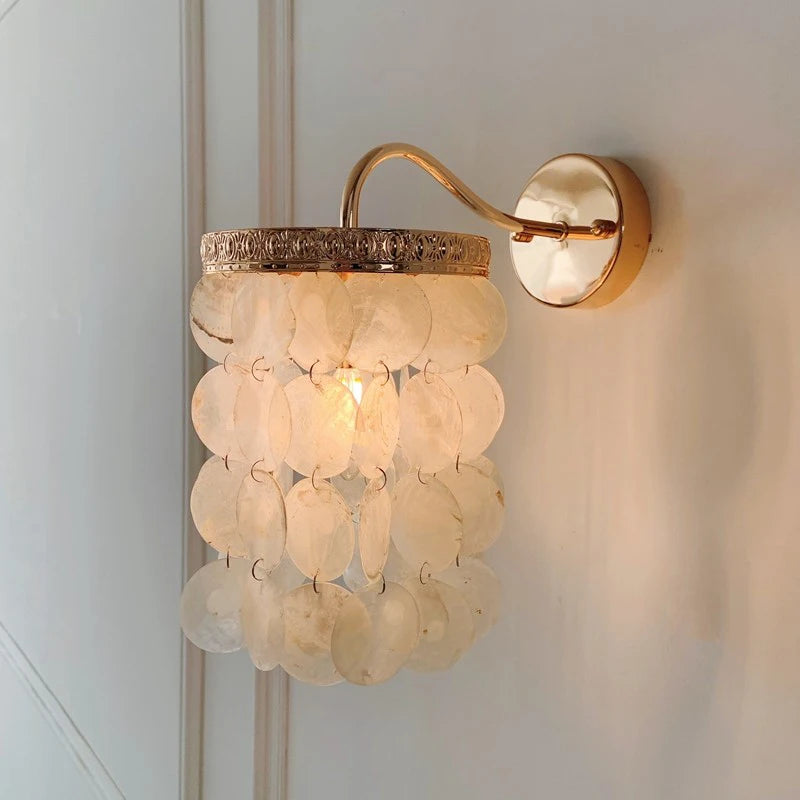Close-up of a gold wall sconce with white shell accents, showcasing the textured metal rim and mounting plate.