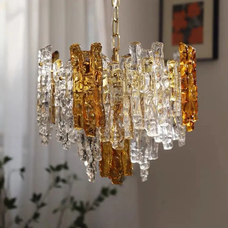 A glass tube chandelier with amber and clear glass elements suspended by a metal chain, showcasing its textured design against a softly lit room.