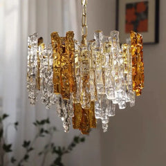 A glass tube chandelier with amber and clear glass elements suspended by a metal chain, showcasing its textured design against a softly lit room.