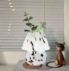 White lamp with black spots on a box next to a wooden bear toy, with a blurred window in the background.