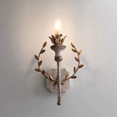Distressed gold metal wall sconce with a leaf wreath design and a single candle-style light, mounted on a light blue wall.