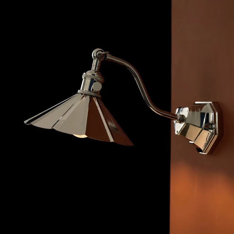 A wall sconce with a metallic, folded-petal-like shade in a chrome finish, casting warm light on a dark background.