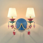 Gold wall sconce with white fabric shades and colorful beaded and flower-like accents, mounted on a blue backing plate.