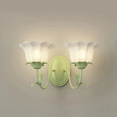 Close-up of a green floral wall sconce with two frosted glass shades, mounted on a neutral wall.