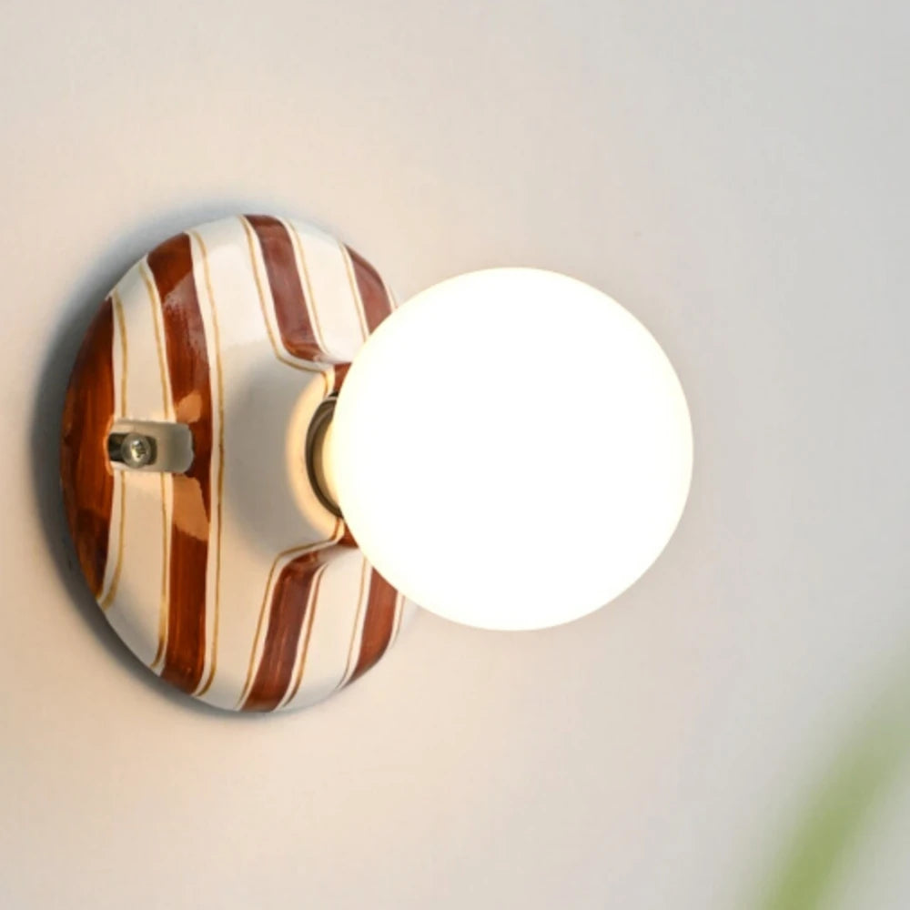 Ceramic wall sconce with brown and white stripes and a glowing round bulb.