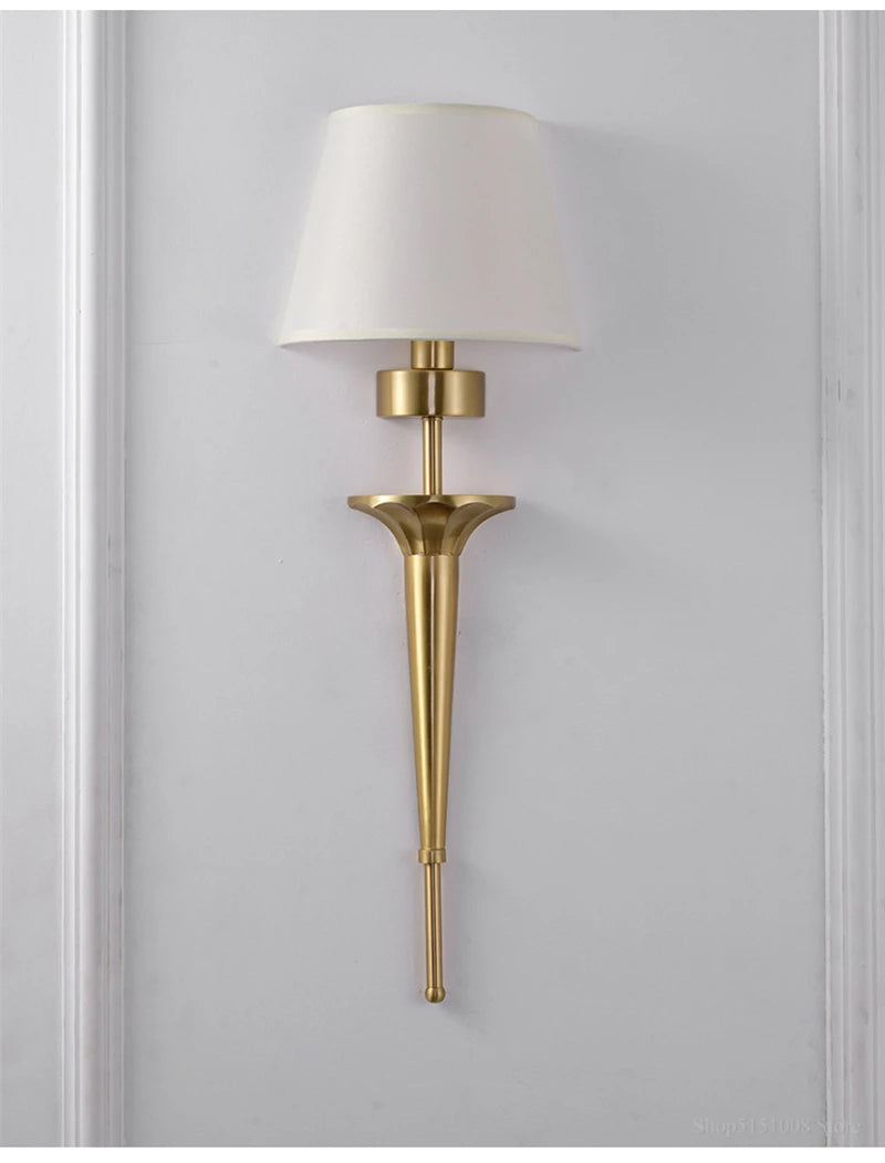 Gold wall sconce with a white lampshade on a gray wall