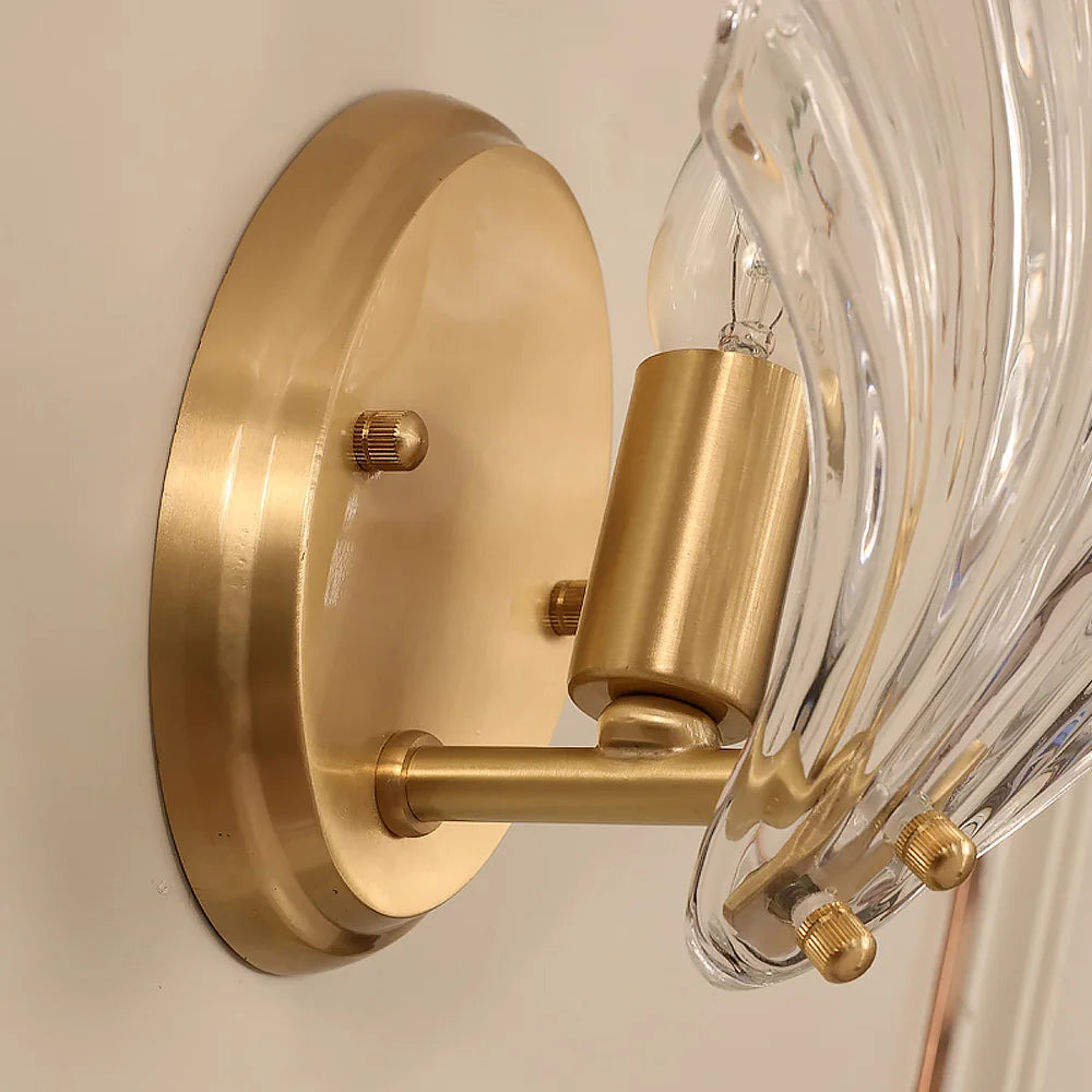 Close-up of a gold wall-mounted light fixture with clear glass shade.