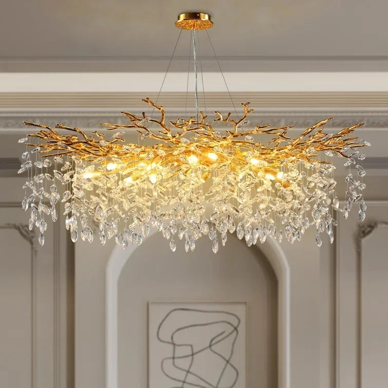 Chandelier with gold branch design and crystal accents in a room with white walls and abstract art.