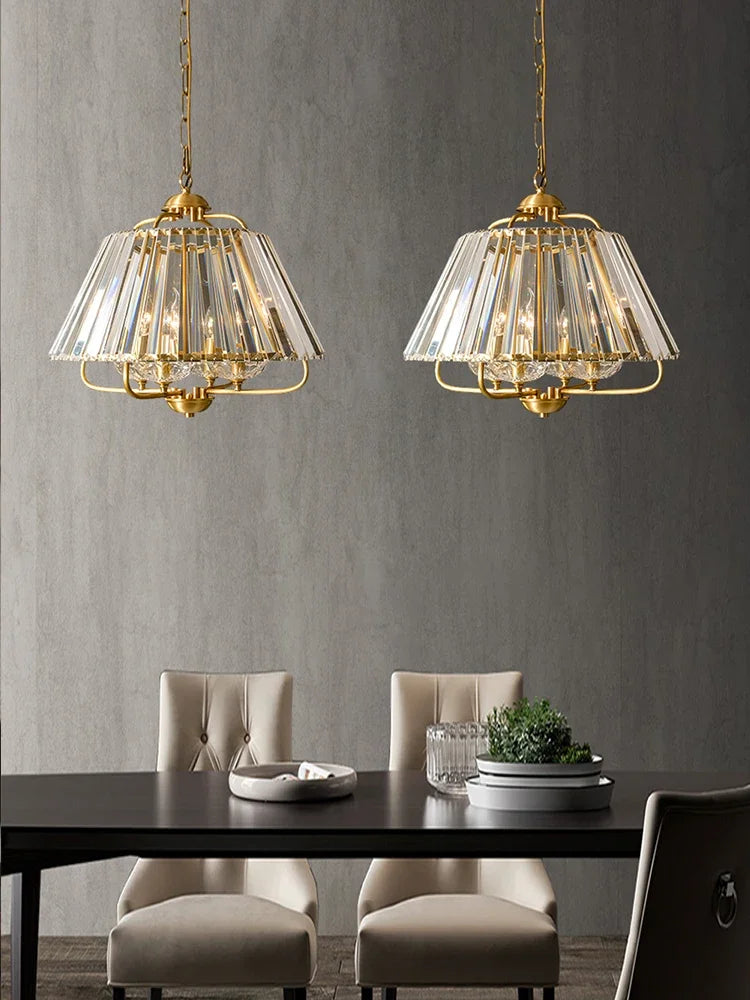Two gold crystal faceted pendant lights hanging above a dining table with beige chairs.