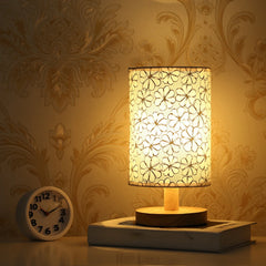 Linen drum shade table lamp with a floral pattern on a wooden base, shown with a white alarm clock on a stack of books.