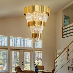 Gold chandelier hanging in a room with large windows and a staircase.