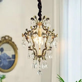 A gold crystal chandelier hanging against a white wall, showcasing its intricate design and crystal droplets.