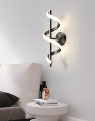 Modern wall sconce with spiral design on a white wall above a nightstand.