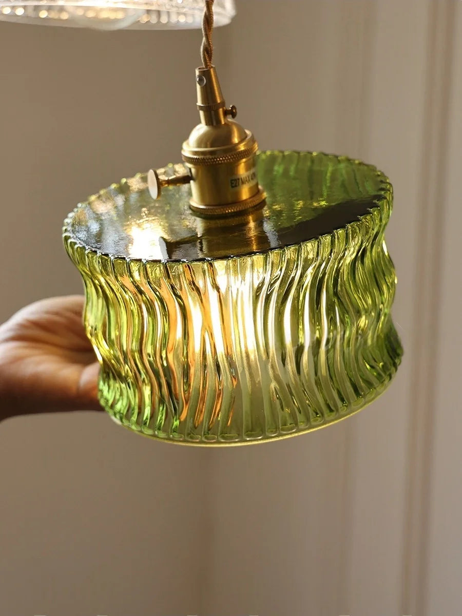 Green glass pendant light with brass fitting against a neutral background