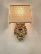 Close-up of a vintage-style wall sconce with a carved wooden base and a light beige fabric shade mounted on a white wall.