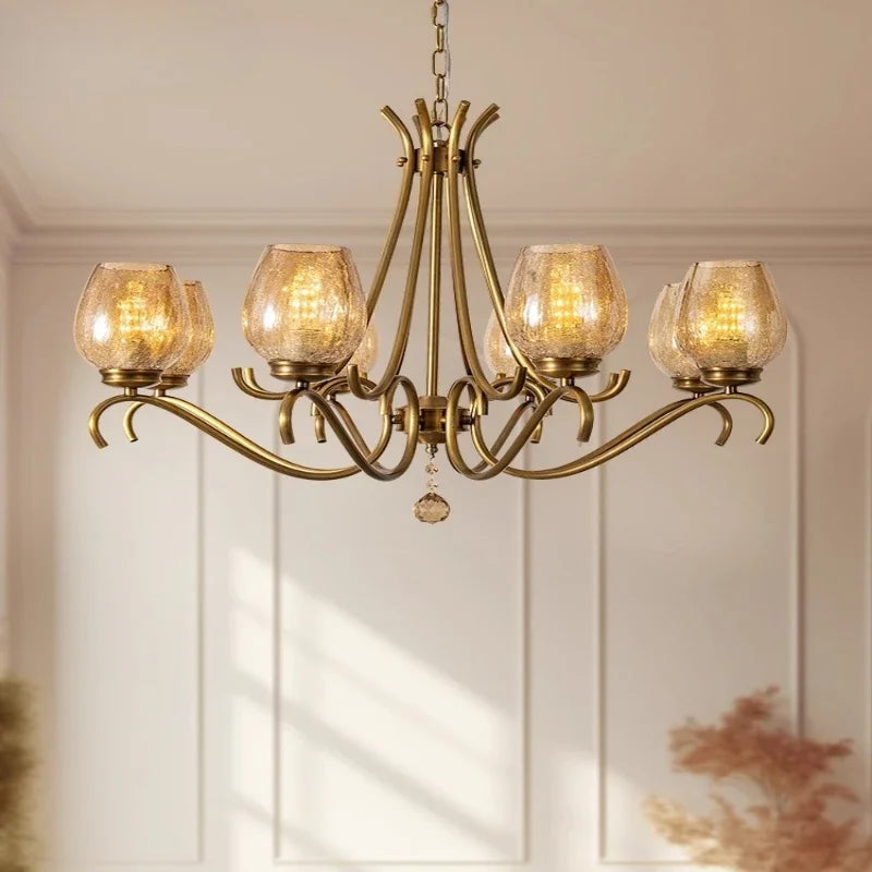 Close-up view of a gold chandelier arm with a seeded glass shade and an illuminated LED bulb.