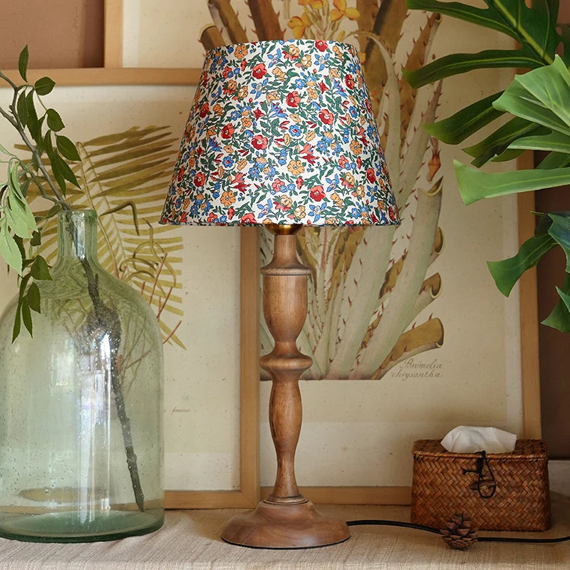 Wooden lamp with a floral fabric shade in a home setting with plants and decor.