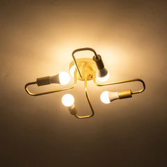 Gold metal starburst semi-flush ceiling light fixture with four lit LED bulbs against a dark ceiling