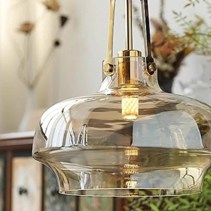 Clear glass pendant light with gold fixture against a blurred indoor background