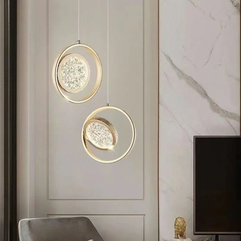 Two gold ring pendant lights with crystal diffusers hanging in a living room setting near a television.