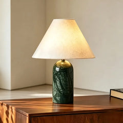 Green stone art ceramic table lamp with a conical fabric shade, illuminated and placed on a wooden surface.