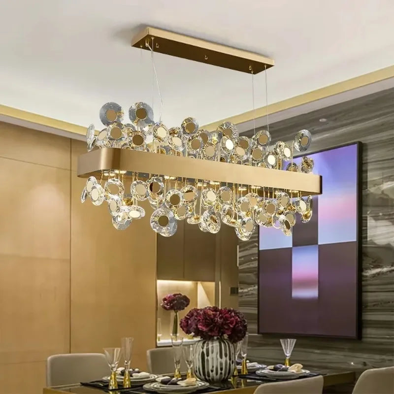 Rectangular gold chandelier with multiple tiers of clear and gold-toned crystals, installed above a dining table.
