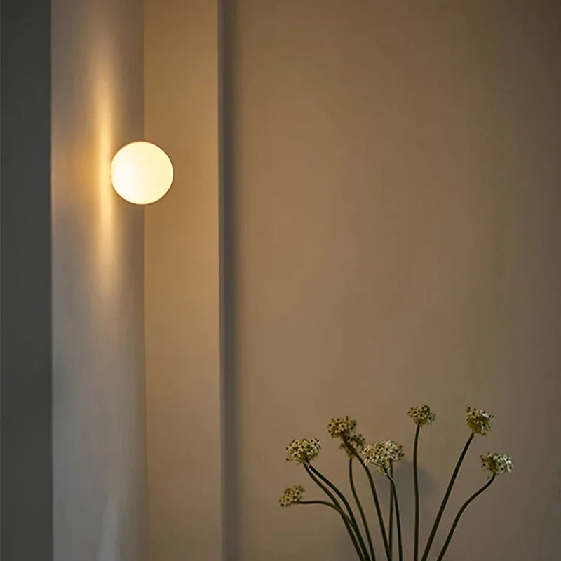 Wall-mounted light fixture casting a warm glow on a wall with a plant in the foreground.