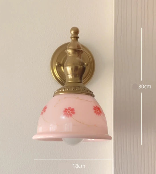 Wall-mounted light fixture with pink glass shade and gold fixture on a neutral wall.