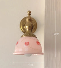 Wall-mounted light fixture with pink glass shade and gold fixture on a neutral wall.