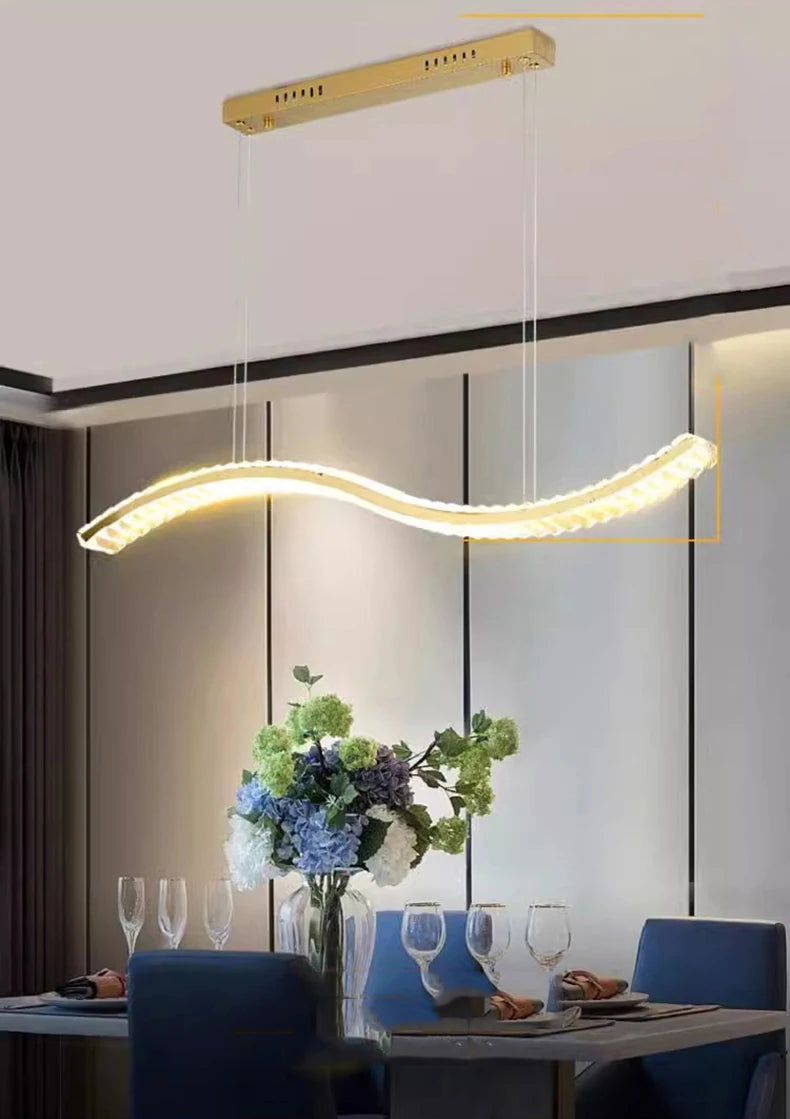 Modern pendant light hanging above a dining table with blue chairs and a floral arrangement.