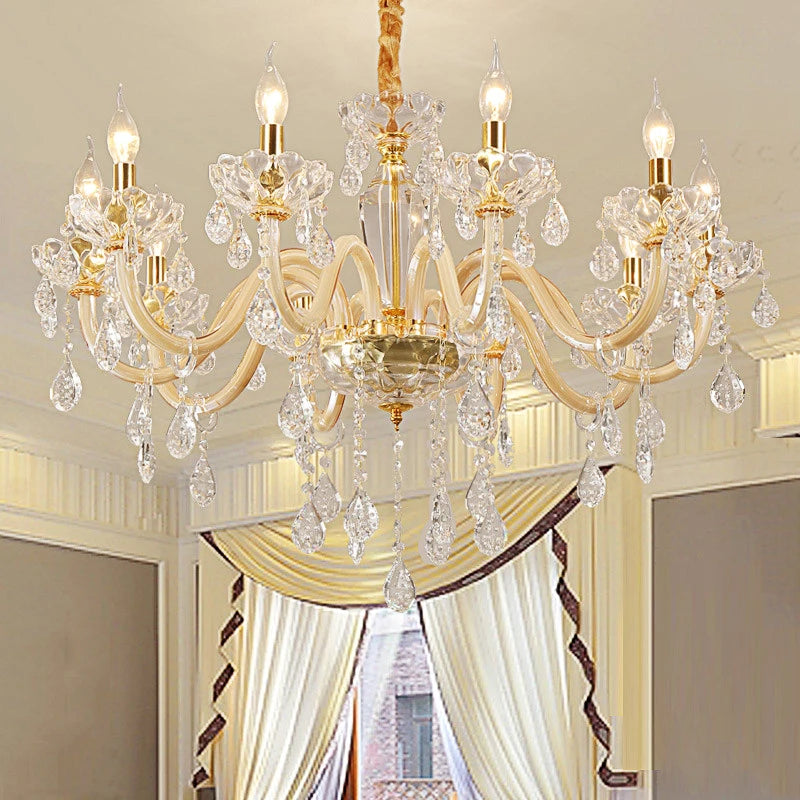 A gold crystal chandelier with multiple arms and dangling crystals, installed in a room with draped curtains.